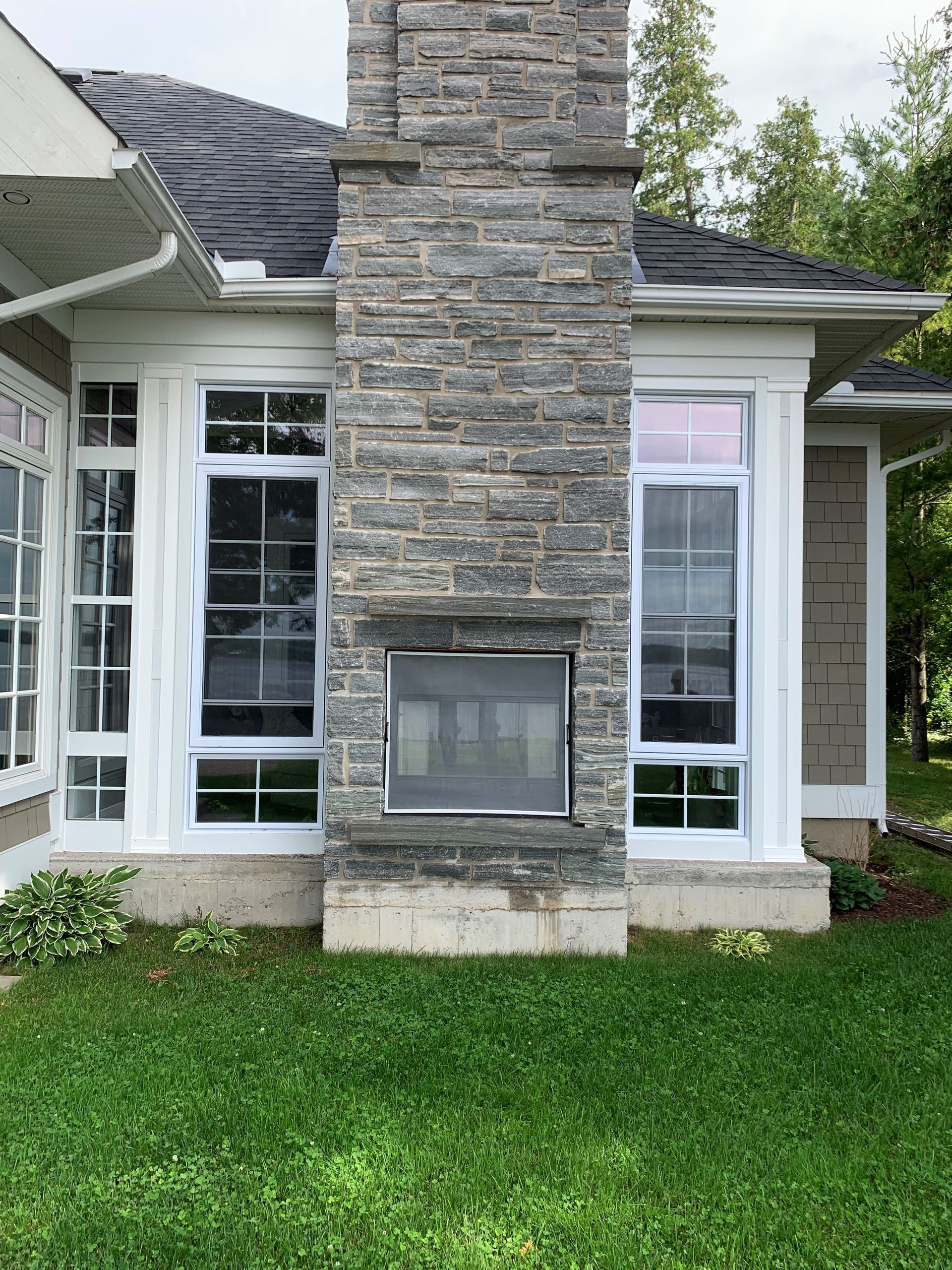 Stone fireplace on an exterior house wall with white trim and tall windows, above a green lawn