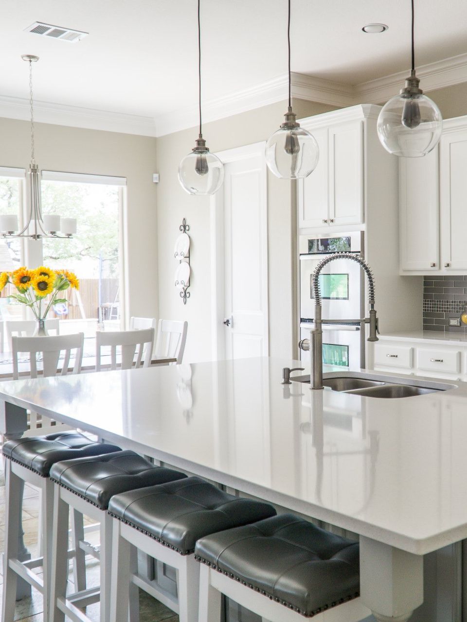 Bright white modern kitchen with island seating, pendant lights, and sunflowers by the window