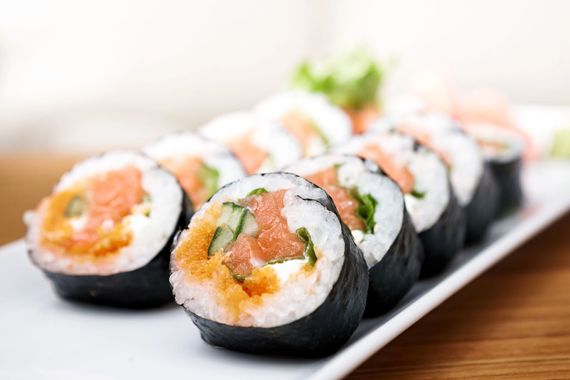 Sushi rolls with salmon and avocado on a white plate, close-up on a wooden table