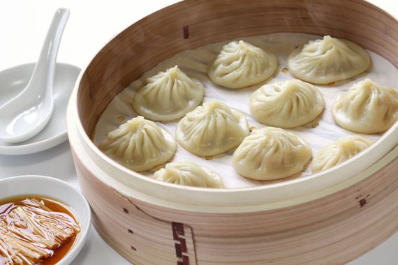 Steamed dumplings in a bamboo basket with dipping sauce and a white spoon on a table