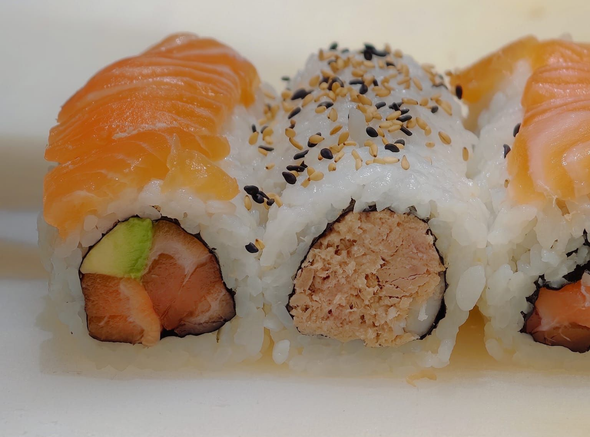 Three sushi rolls topped with salmon, sesame seeds, and a white cream layer on a plate