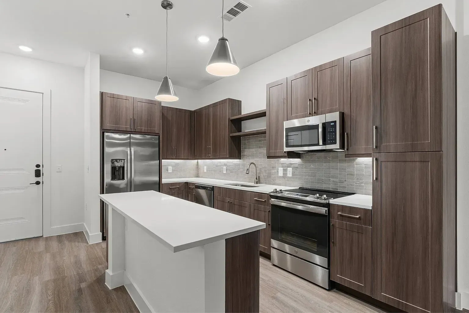 Modern kitchen with dark wood cabinets, stainless steel appliances, and a white island.