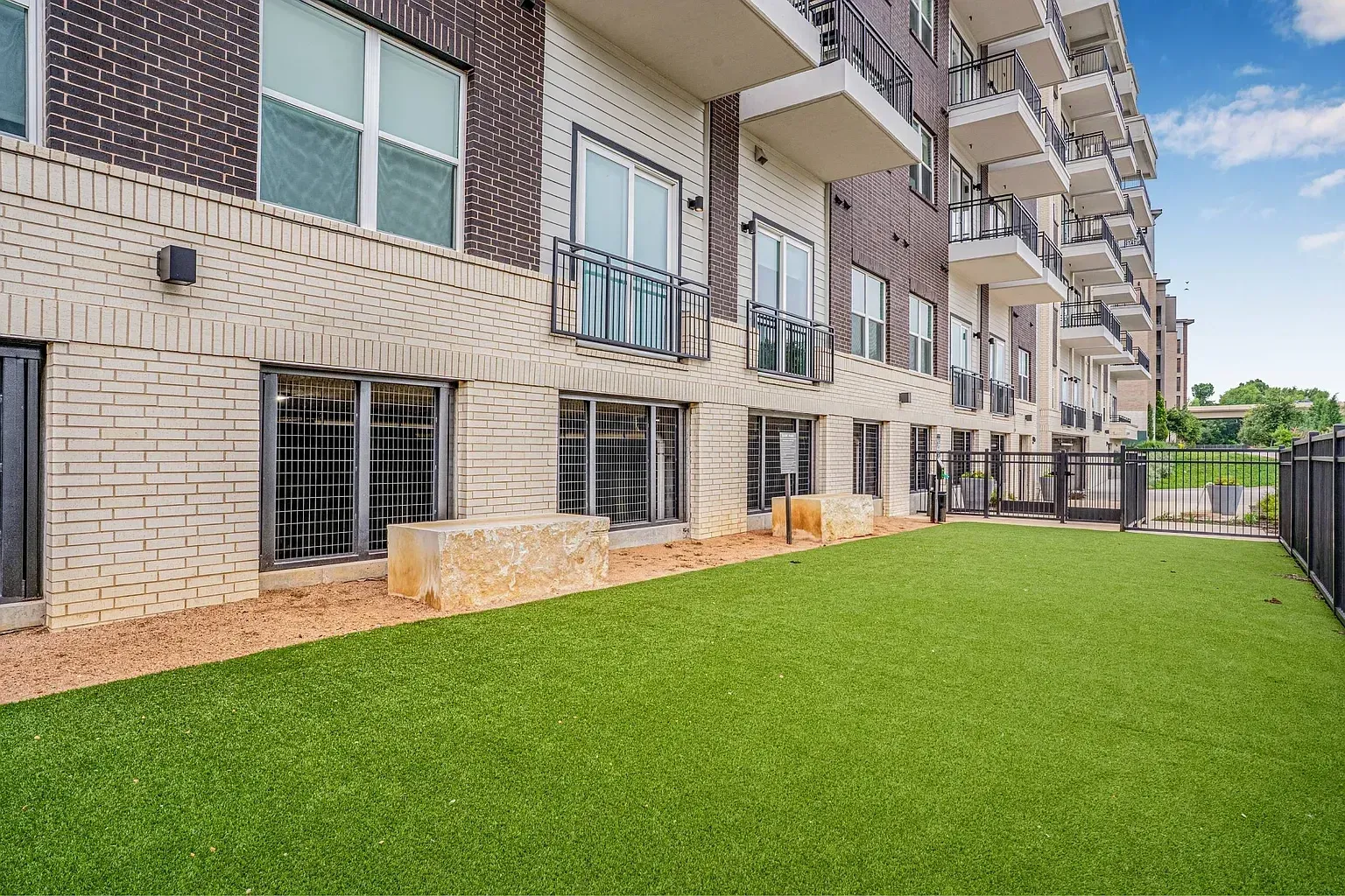 Apartment building exterior with balconies and a fenced-in grassy area.