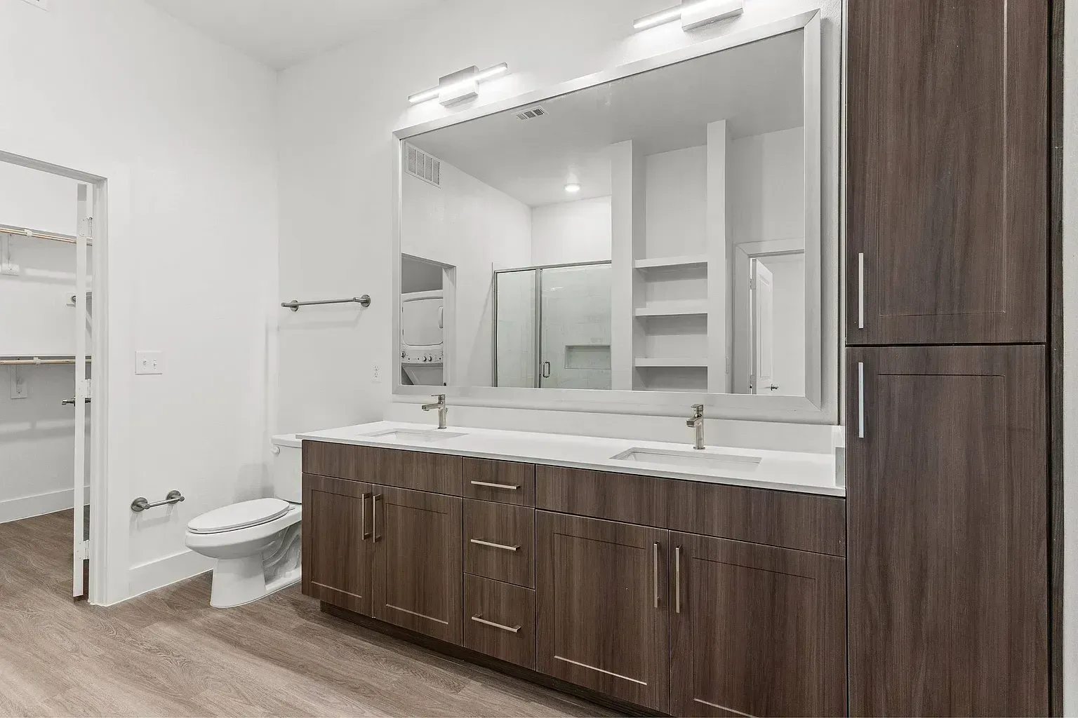 Double vanity with a large mirror, toilet, and washer/dryer visible in closet.