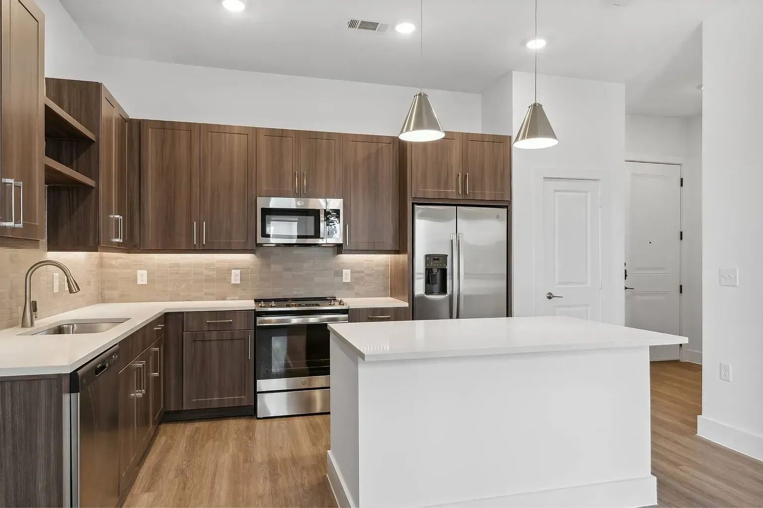 Modern kitchen with dark wood cabinets, stainless steel appliances, and a white island.