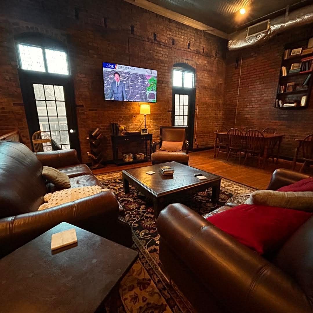 A living room with exposed brick walls, leather sofas, a wooden coffee table, a television, and a dining area.