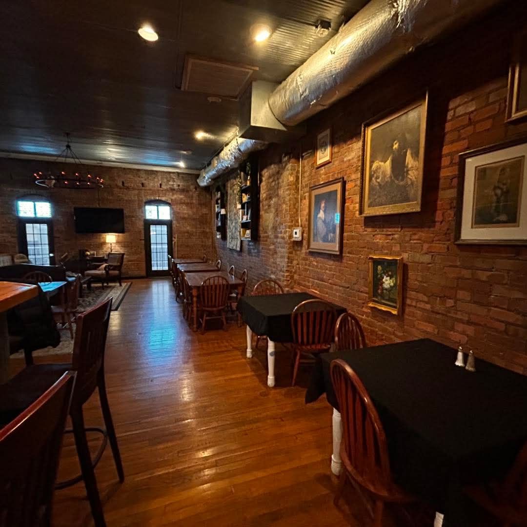 An interior view of a restaurant with wooden floors, brick walls, framed artwork, and tables with black cloths.