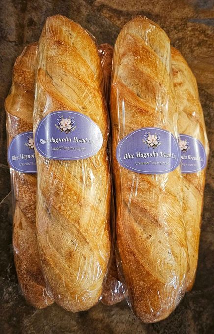Two loaves of bread are wrapped in plastic and sitting on a table.