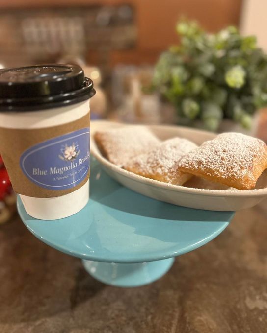 A cup of coffee and a plate of powdered sugar pastries on a cake stand.