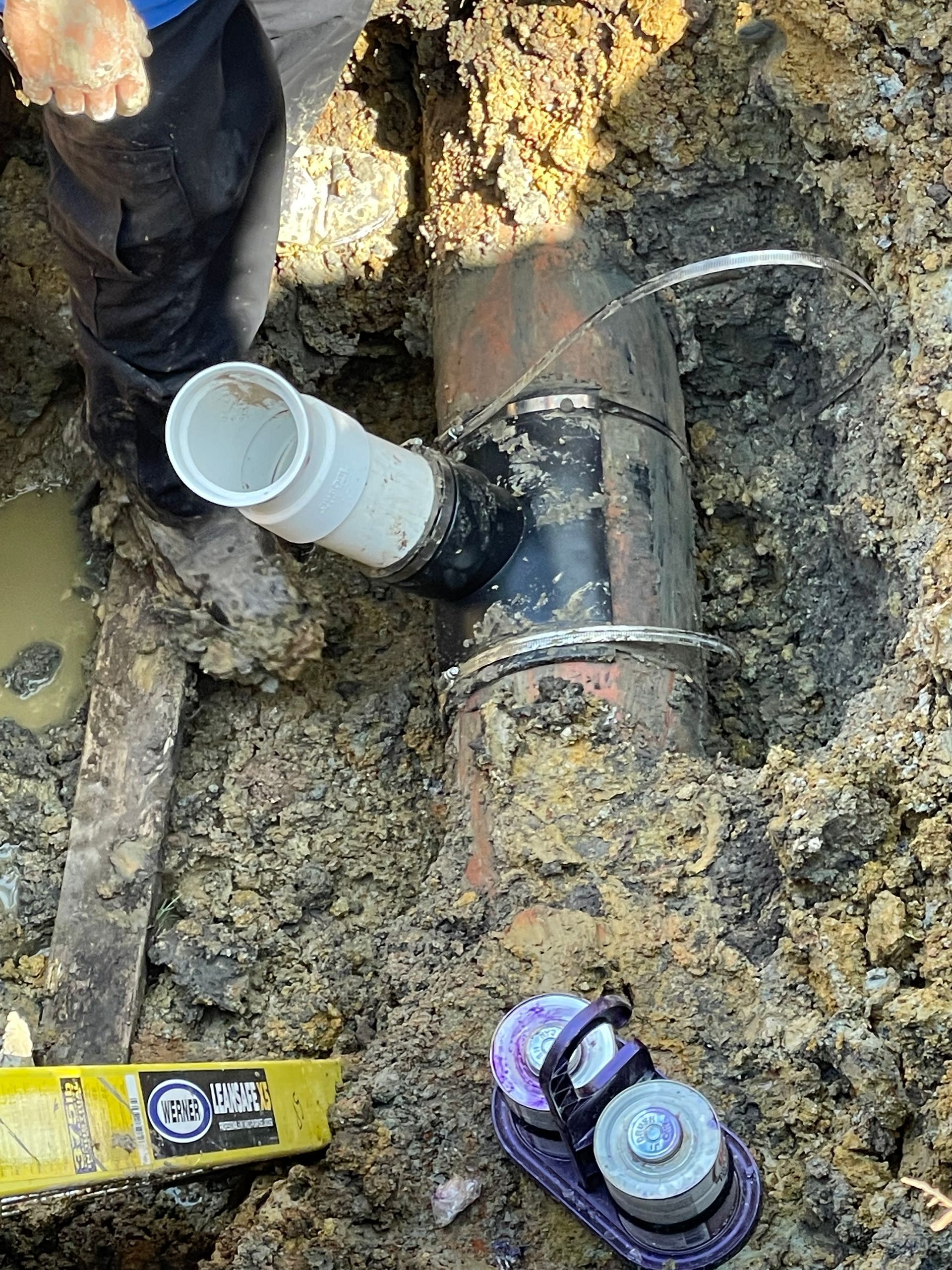 A person is working on a pipe in the dirt.