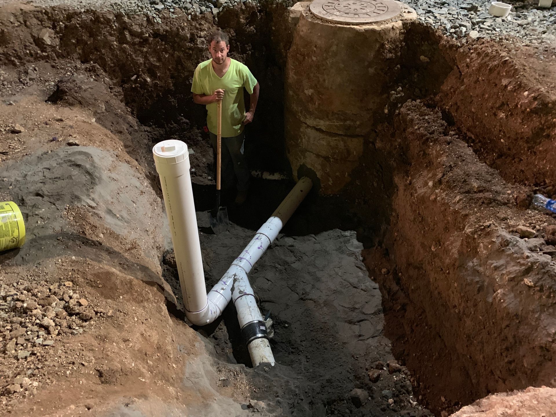 A man is standing in a hole with pipes in it.