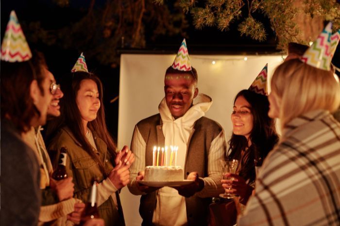 man holding a birthday cake with friends around next to photo booth