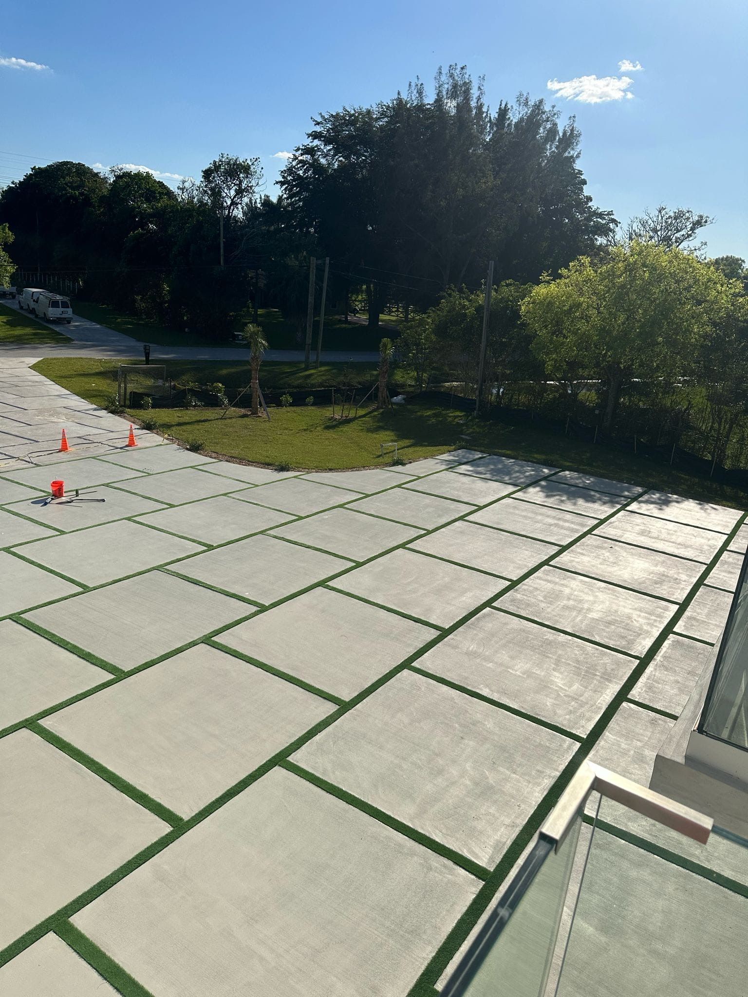 Large light-colored stone patio with green inlays. Trees and road in background under a blue sky.