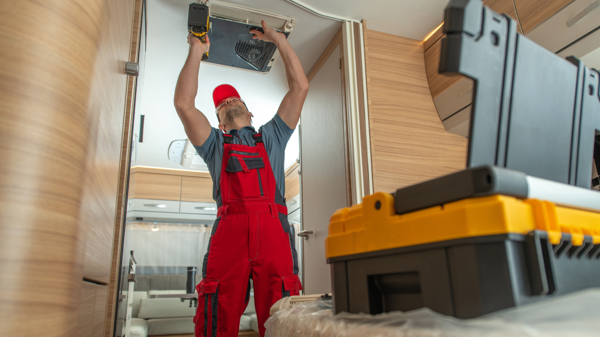 A man in red overalls is working on a camper door.