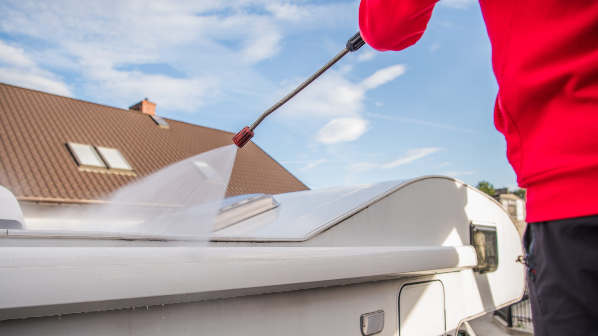A man is using a high pressure washer to clean the roof of a trailer.