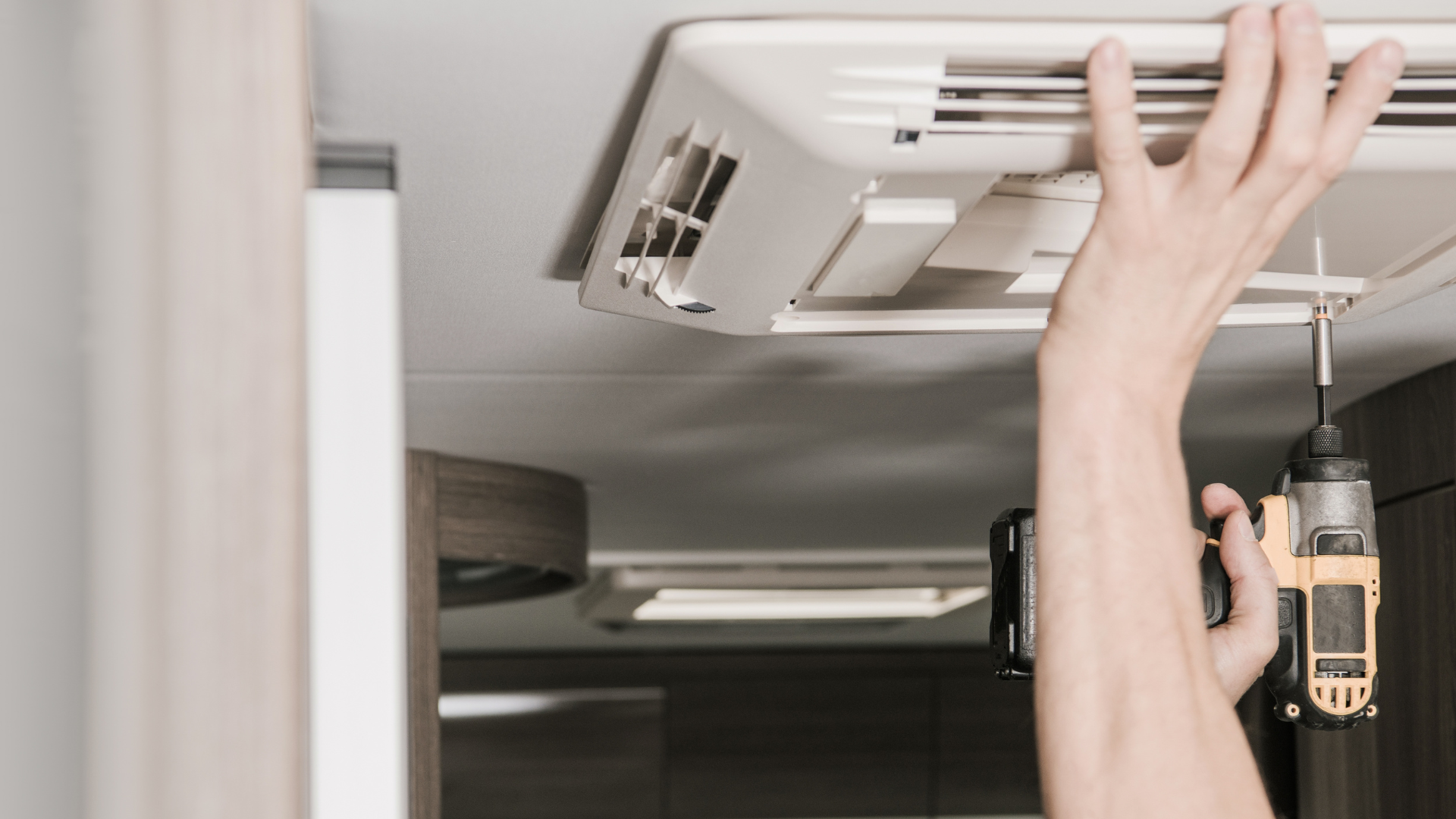 A person is fixing a ceiling fan with a drill.