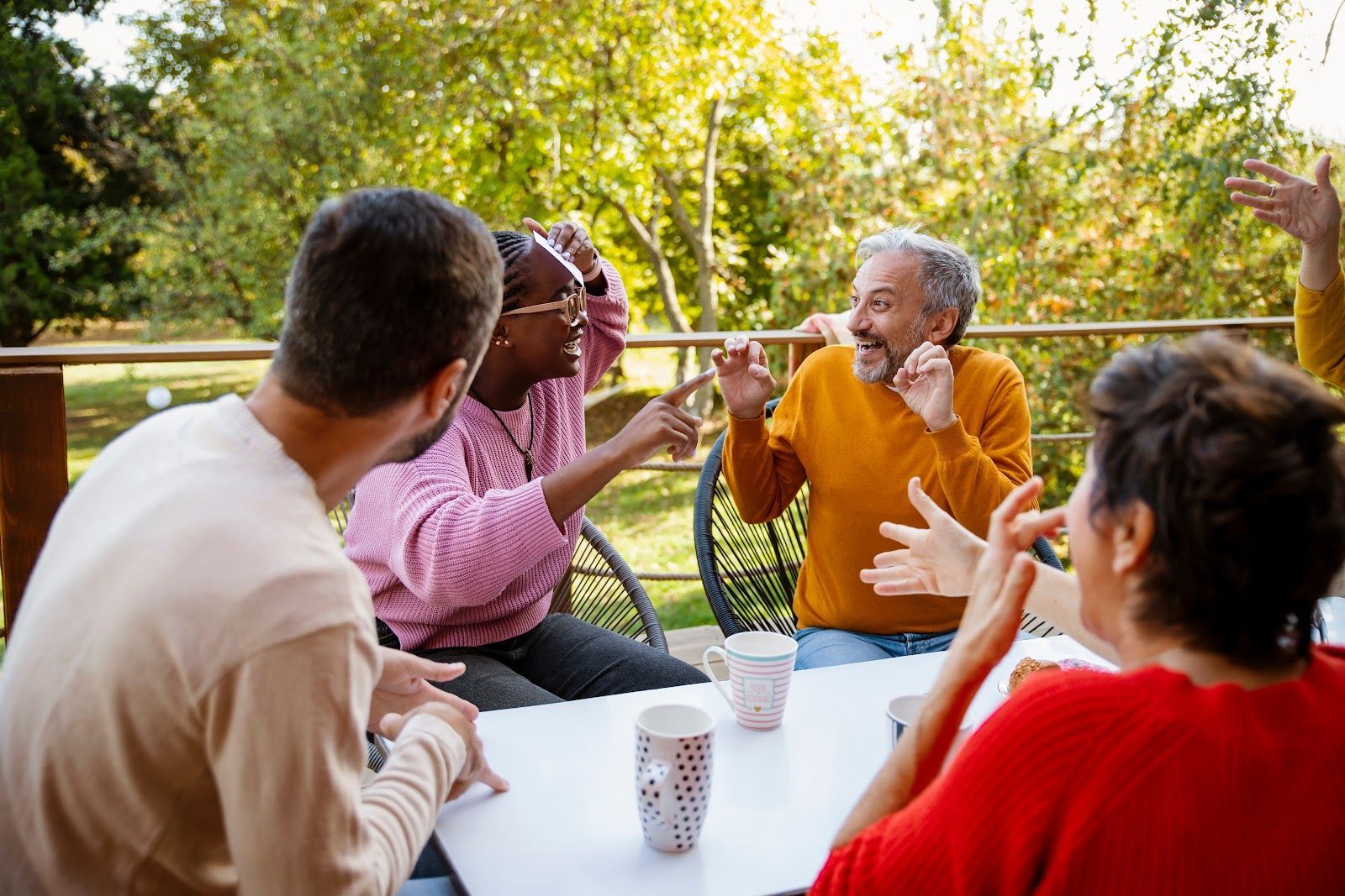 Friends chatting and toasting outdoors at a picnic table in a sunny park