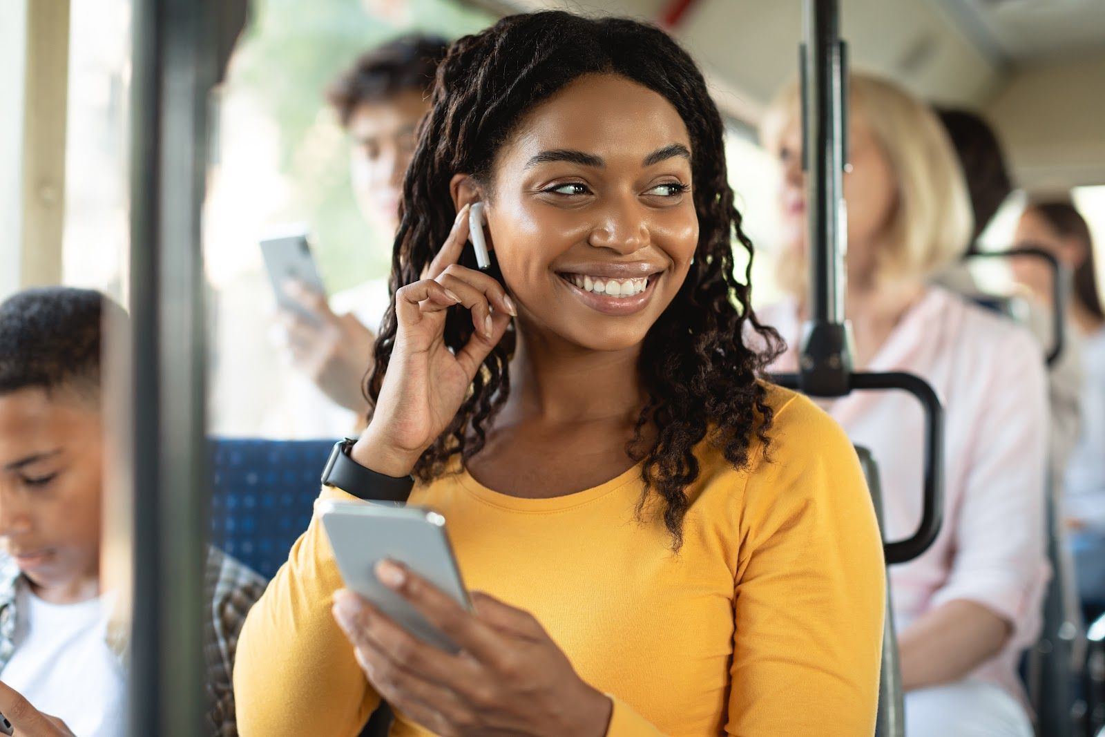 Woman on a bus smiling while talking on a phone and holding a smartphone