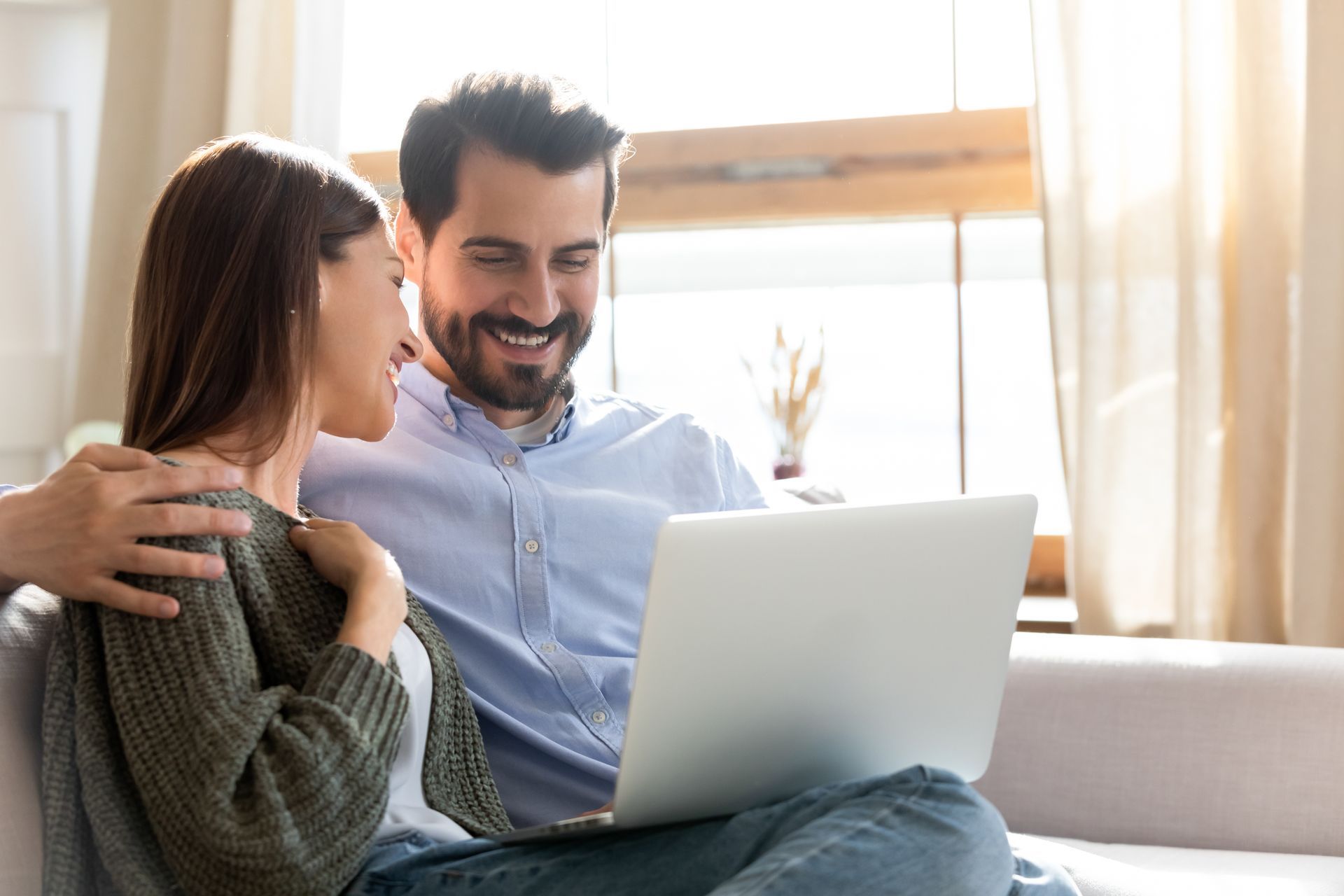 A man and a woman are sitting on a couch looking at a laptop.