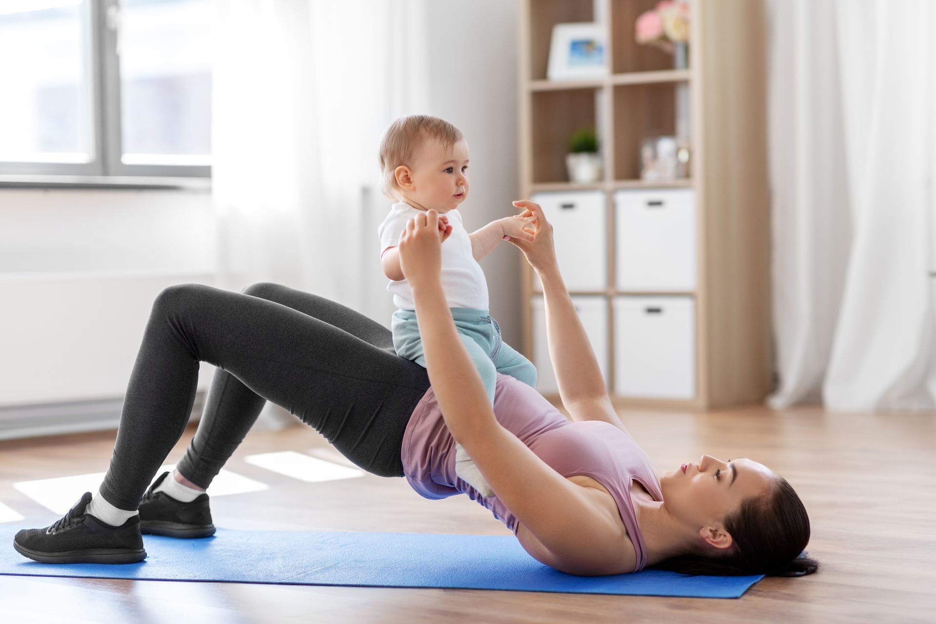 A woman is holding a baby while doing exercises on a yoga mat.
