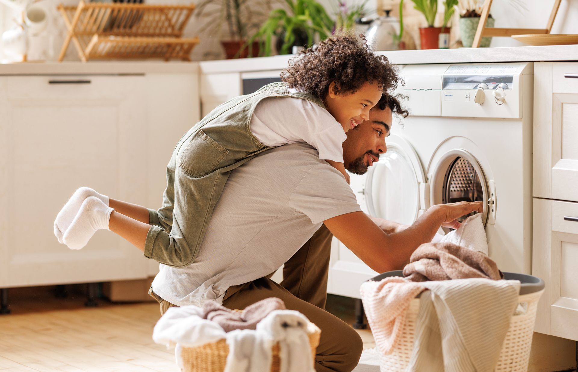 A man and a little girl are doing laundry in a kitchen.