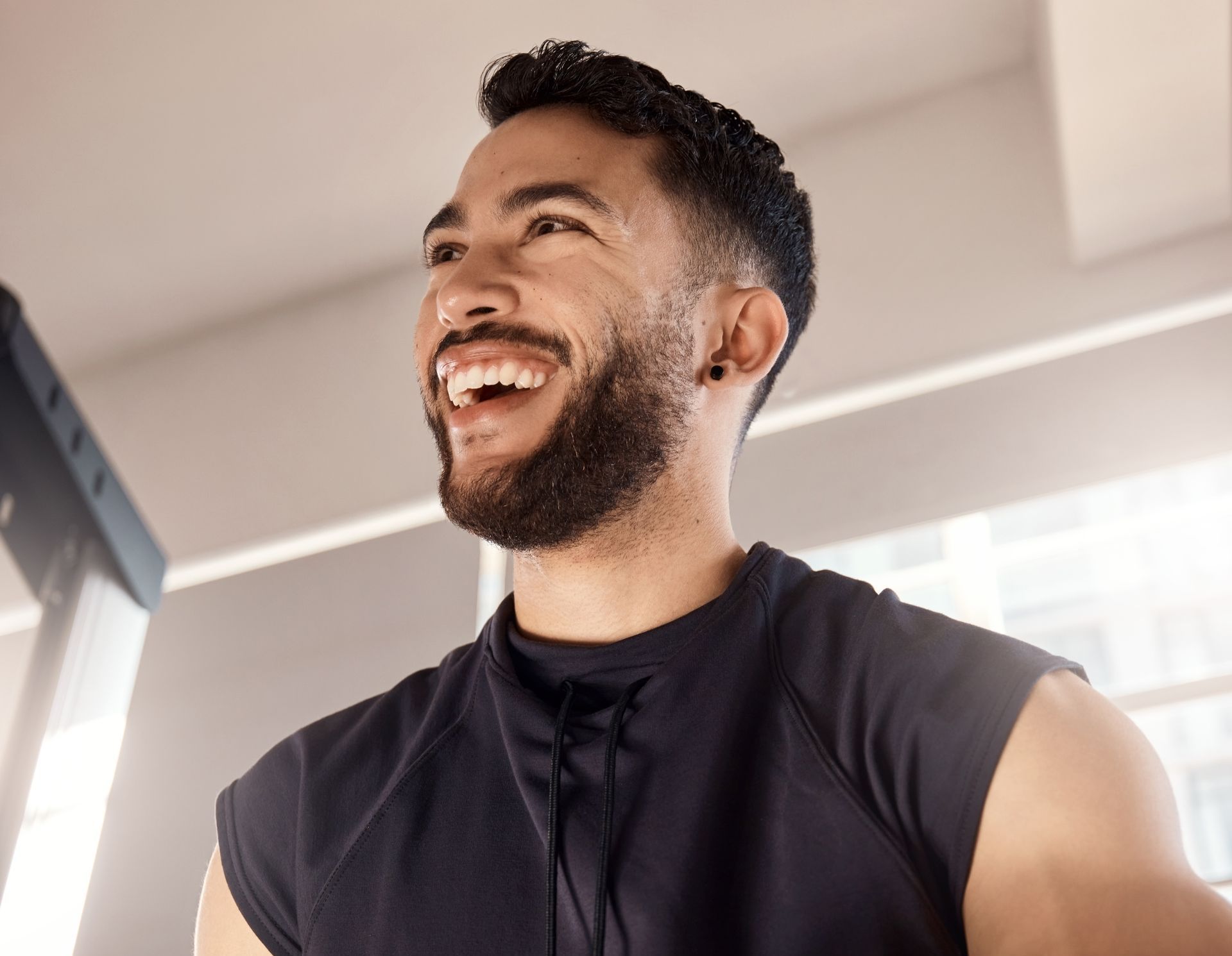 A man is laughing while looking at his watch in a gym.