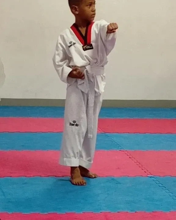Niño con uniforme blanco de artes marciales en posición de guardia sobre una estera azul y roja.