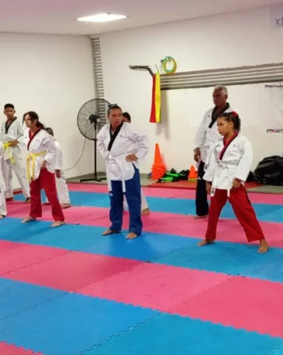 Clase de artes marciales practicando posturas sobre colchonetas azules y rosas en un estudio.