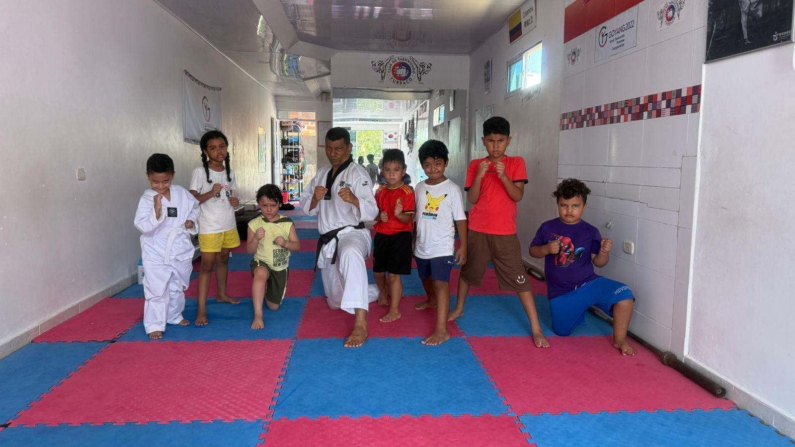 Niños practicando sobre colchonetas en un estudio de artes marciales, haciendo fila con un entrenador.