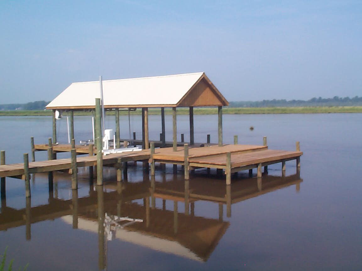 Wooden dock with shelter on calm water, reflected in the water.