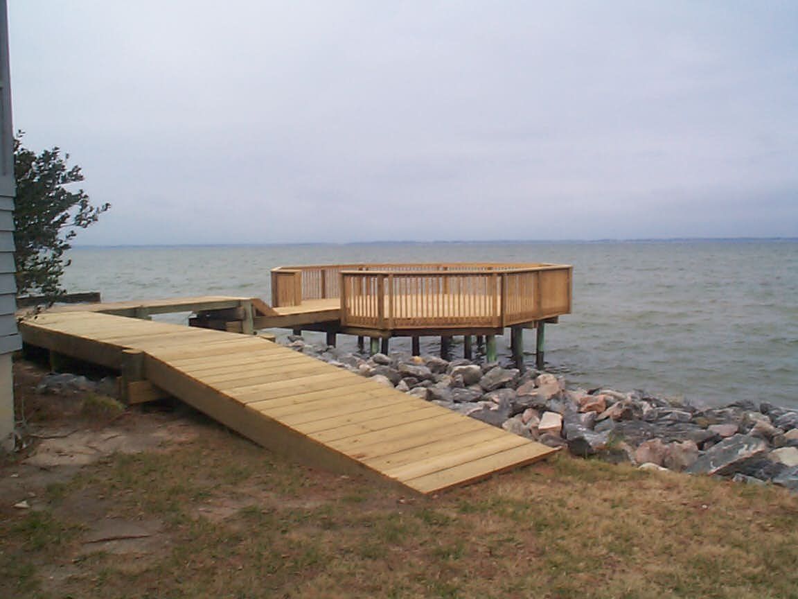 Wooden deck and ramp leading to an elevated platform over a rocky shoreline, overlooking a body of water under an overcast sky.