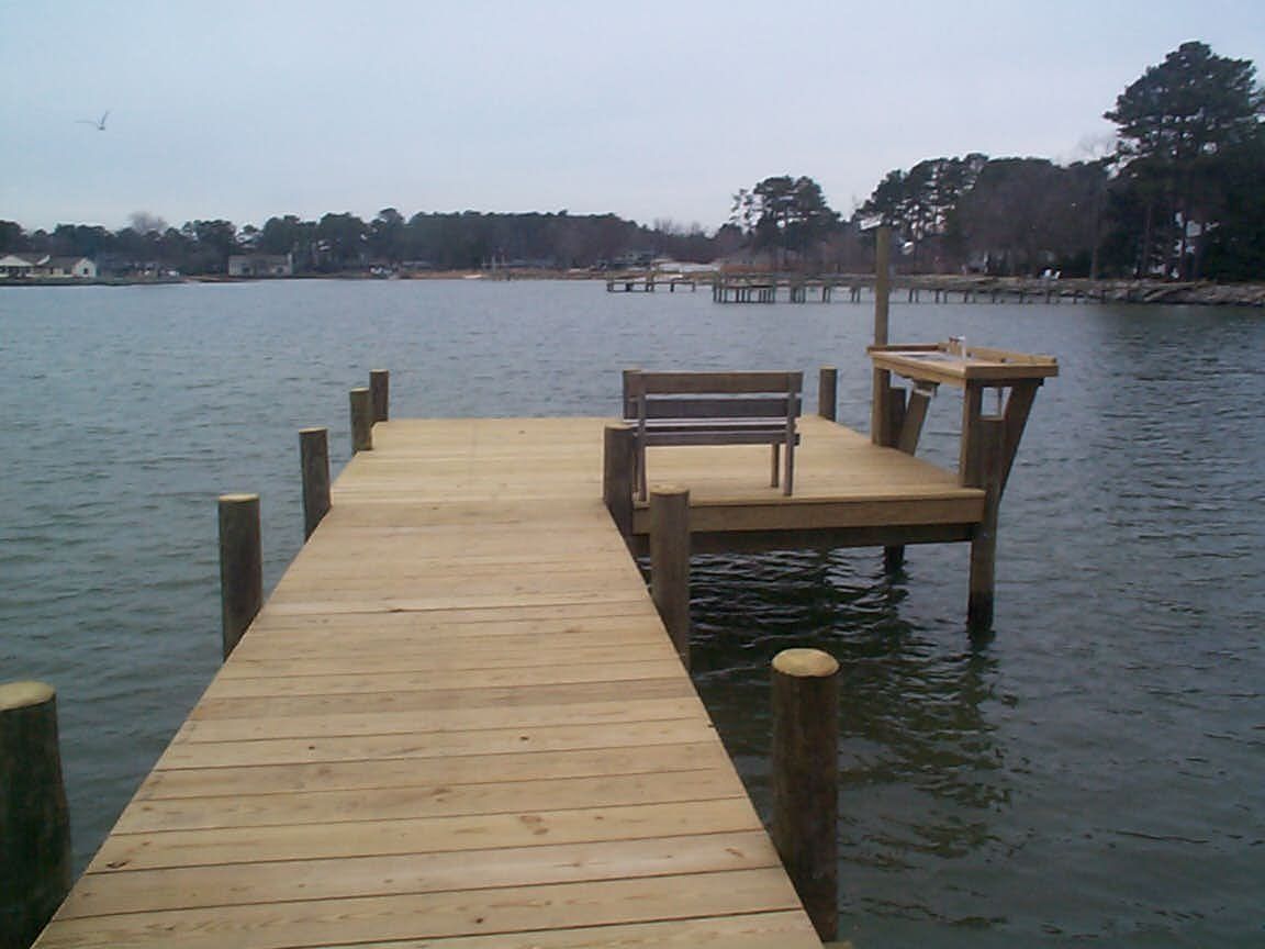 Wooden dock extending into water with a bench and a small table on the end; overcast sky.