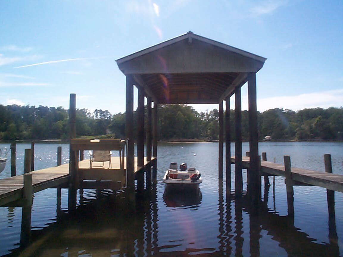 Boat in a covered boat slip on a lake, surrounded by docks. Bright blue sky overhead.