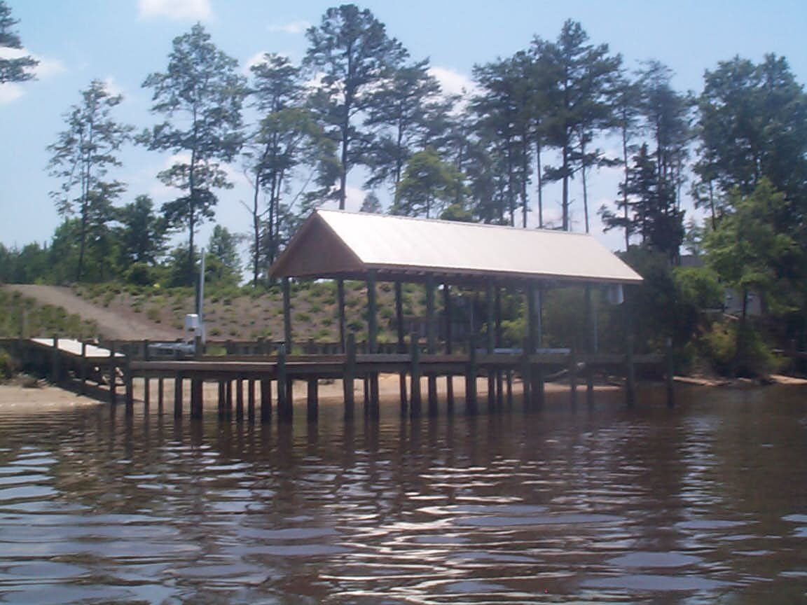 Dock with covered shelter over water, trees in background, sunny day.