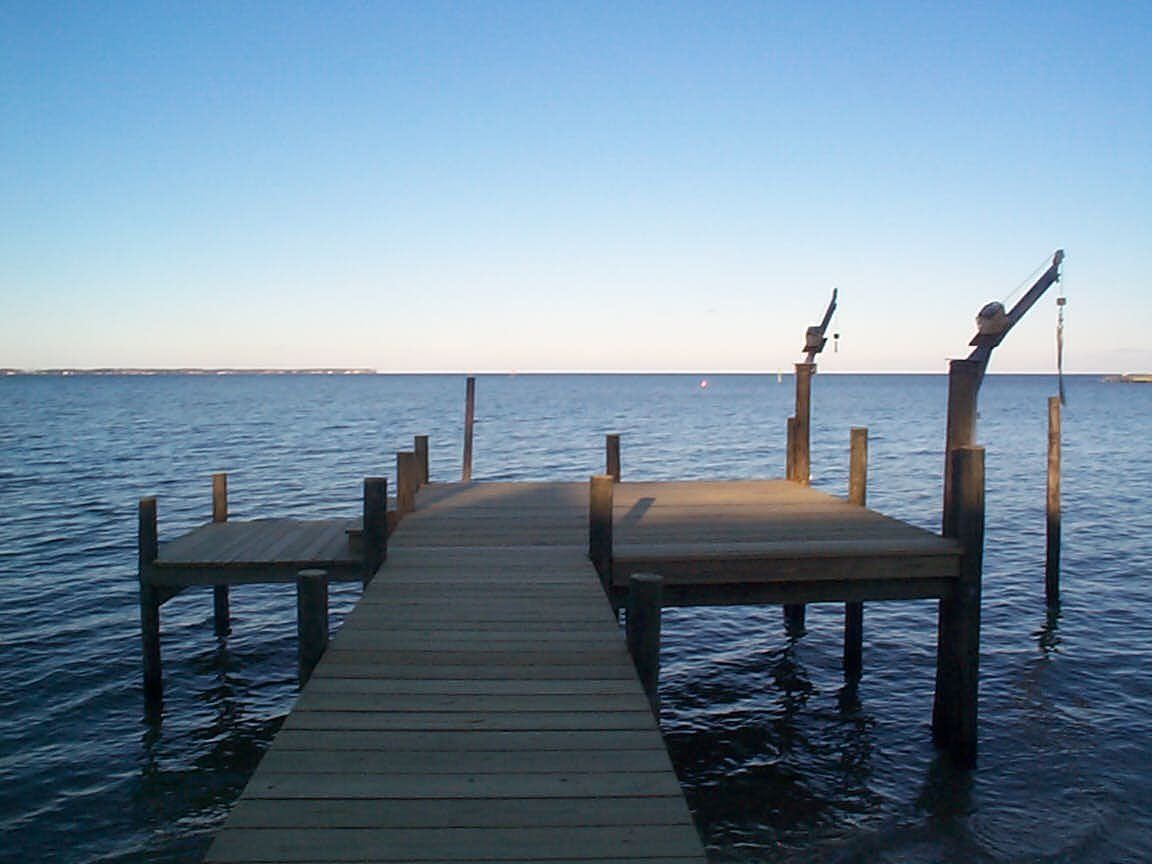 Wooden pier extending into calm water under a clear blue sky.