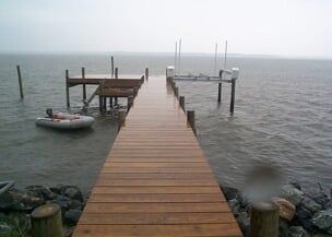 Wooden pier extending into gray water on an overcast day. A small inflatable boat is tied to the side.