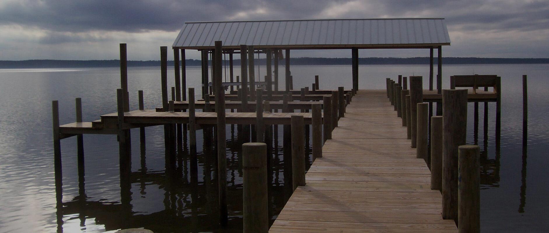 Wooden pier extending into calm water under a cloudy sky.