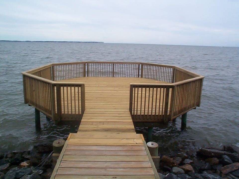 Wooden pier leading to an octagonal deck over water, surrounded by railing, on a cloudy day.