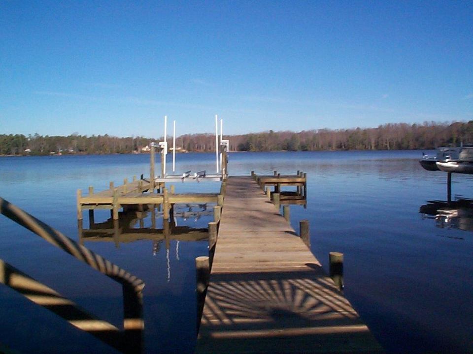 Wooden dock extends into calm lake under a clear blue sky, with trees in the background.