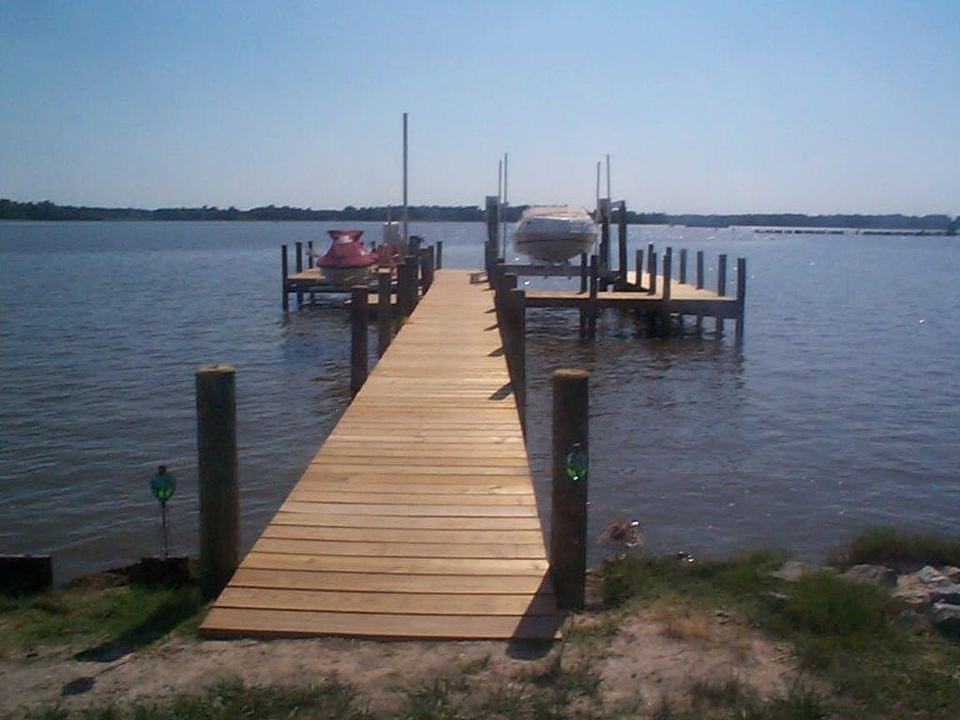 Wooden pier extends into a calm body of water; a boat and jet ski sit at the end.
