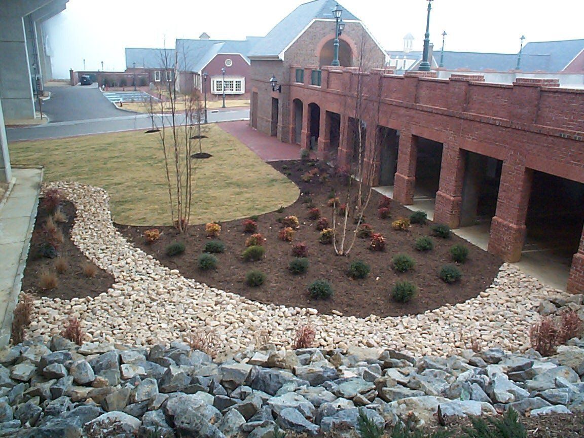 Newly installed commercial landscape bed with young shrubs, mulch, and decorative river rock