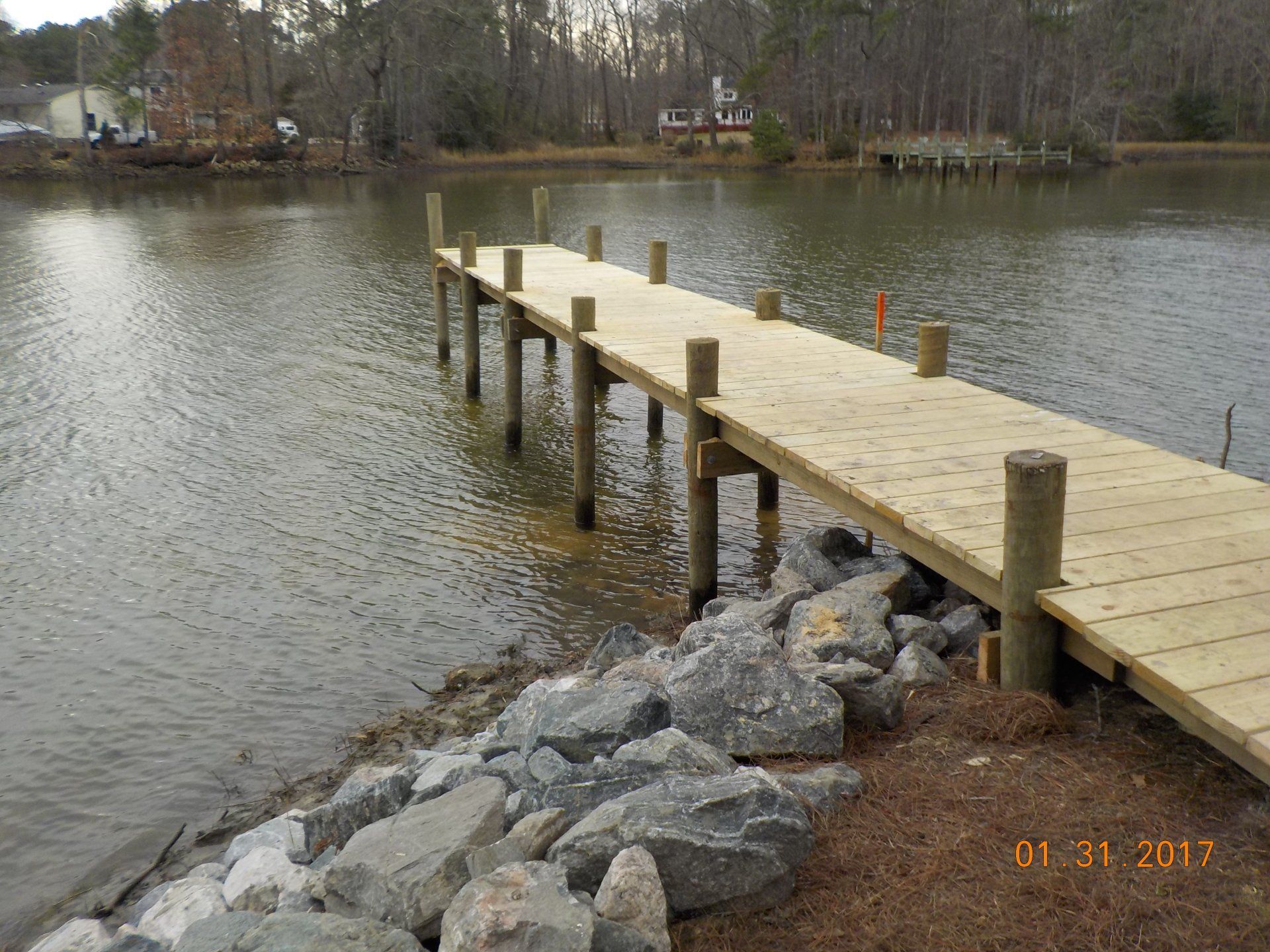Wooden pier extends over a lake, with stone breakwater at the shore.