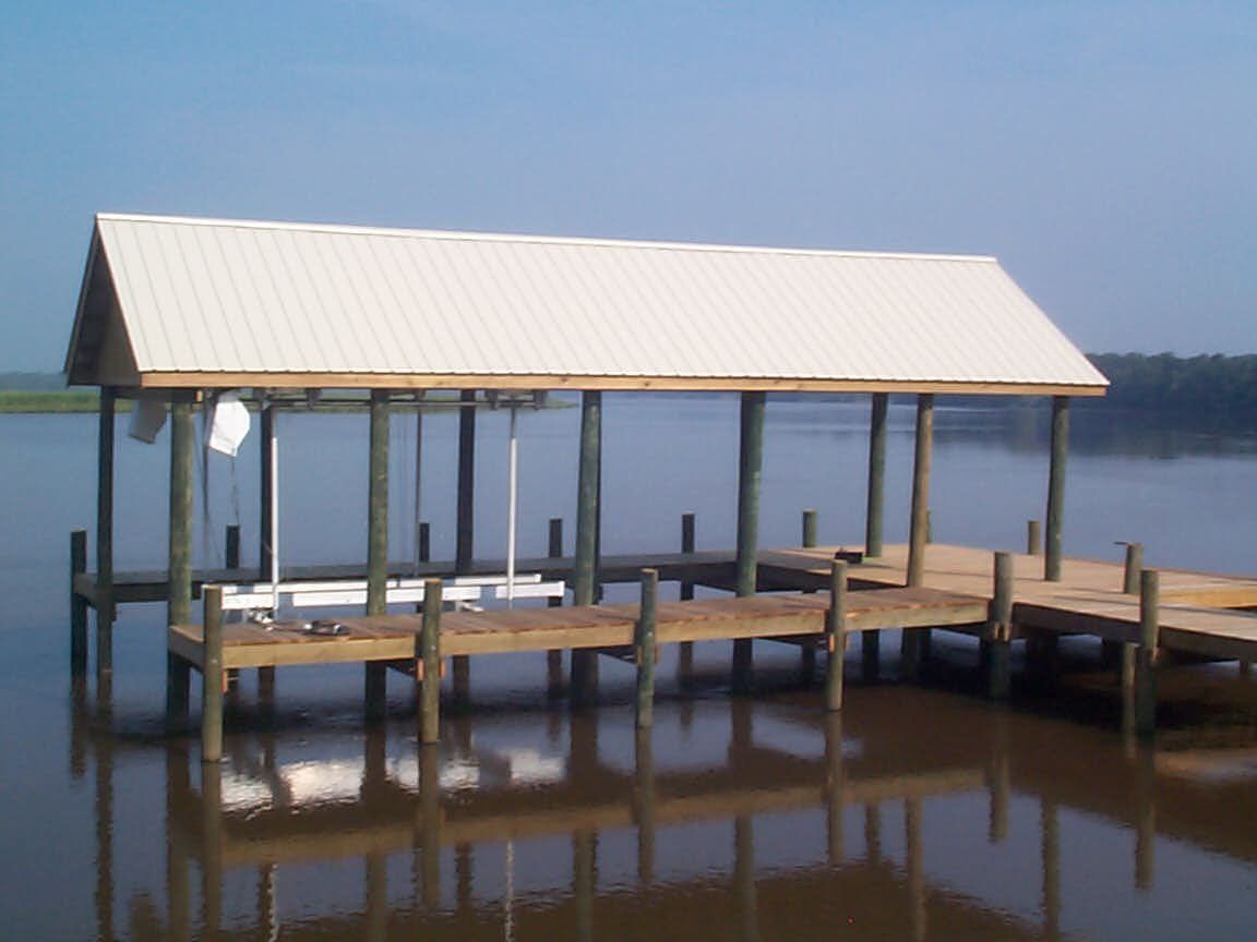 Wooden dock with a white-roofed boat shelter over the water; reflective surface.