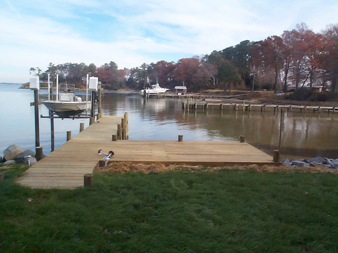 Wooden pier extends into calm water, with a boat lift and boats visible, trees in background.
