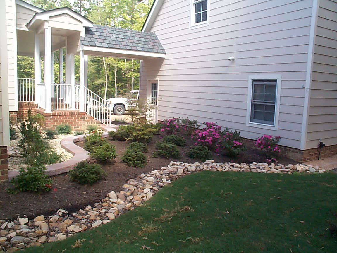 Landscaped house exterior with a curved stone border, flower beds, and porch.