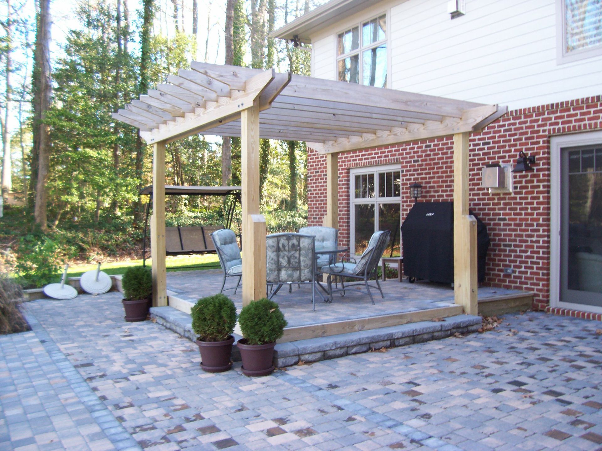 Patio with brick house, pergola, seating, and potted plants on a brick paver surface.