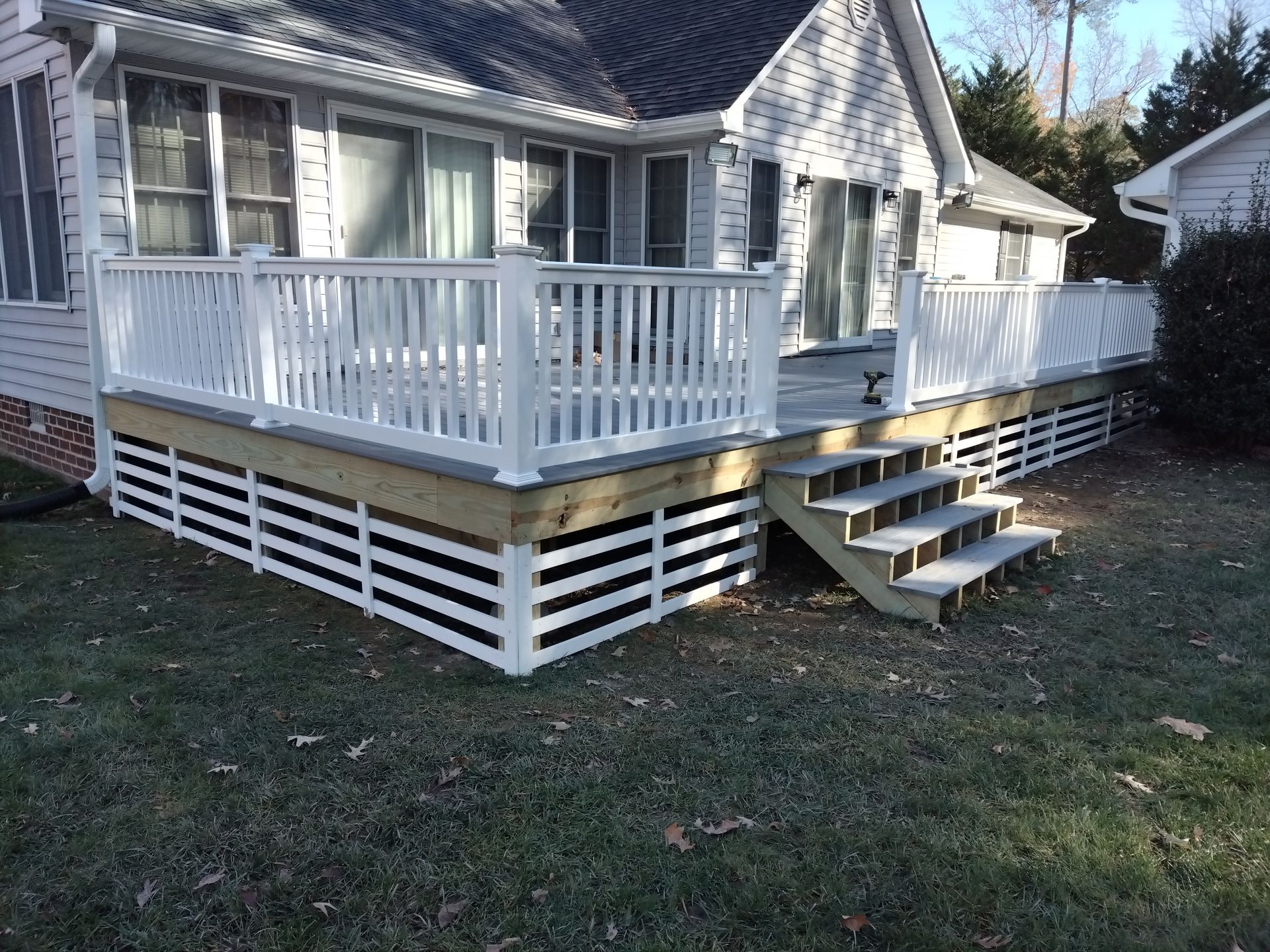 White deck with stairs, built against a light gray house. The deck has white railing and skirting.