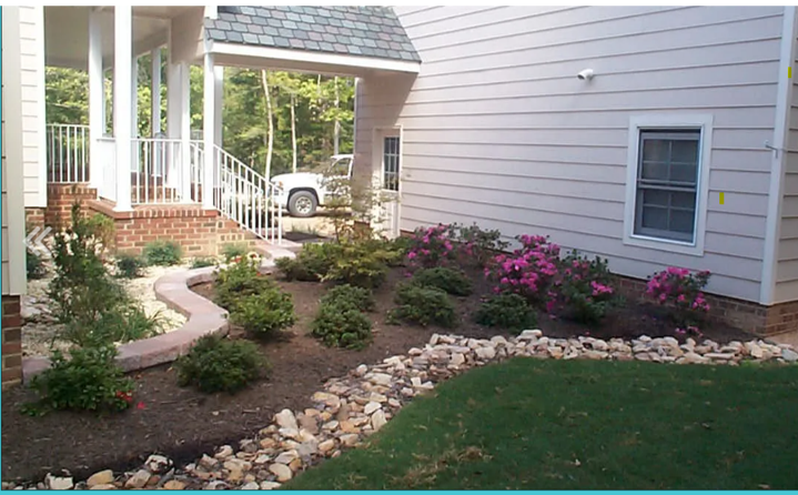 Landscaped front yard with flowering shrubs, stone border, and brick porch steps.