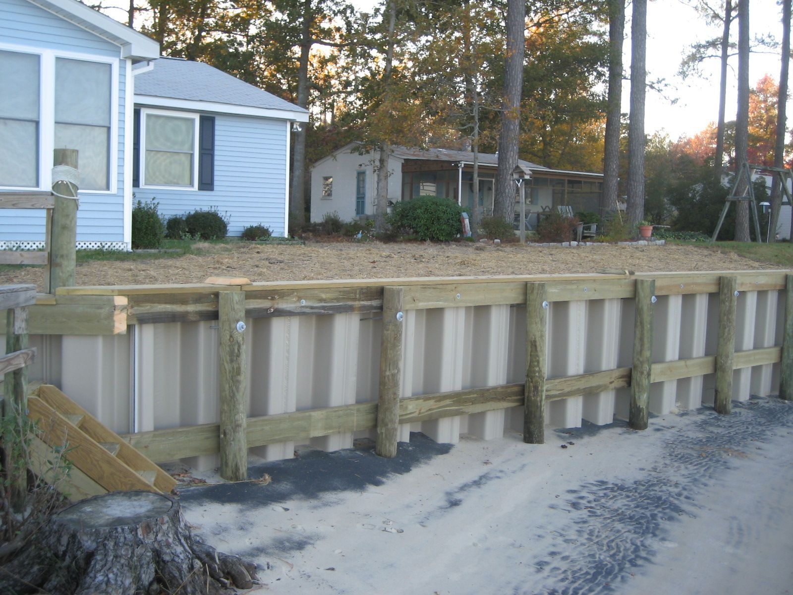 A metal and wood seawall protects waterfront property; houses in background.