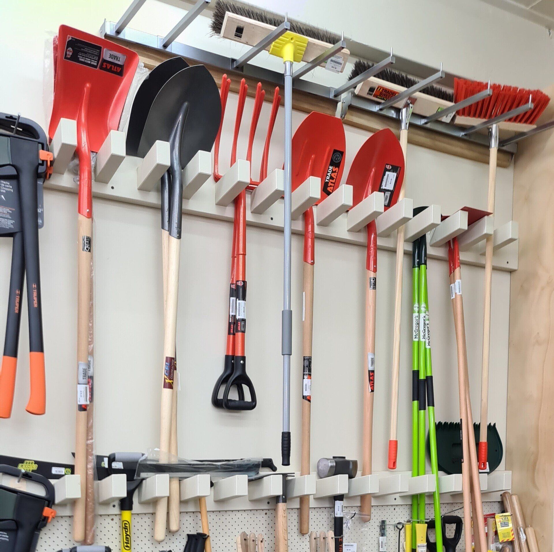A variety of garden tools, including shovels, rakes, and a pitchfork, are organized on a wooden wall-mounted rack.
